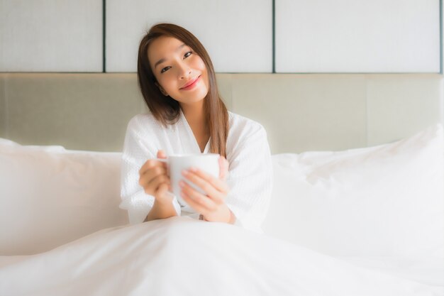 Portret piękna młoda azjatykcia kobieta z filiżanką w sypialni