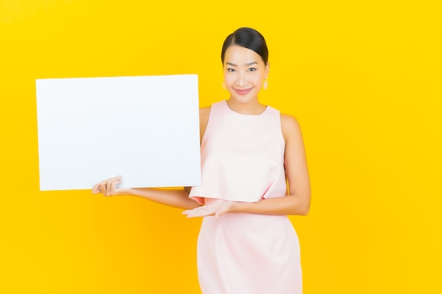 Portret piękna młoda azjatykcia kobieta z pustym białym billboardem na żółto