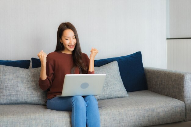 Portret piękna młoda kobieta azjatyckich używać laptopa na kanapie we wnętrzu salonu