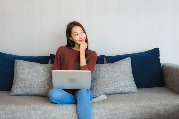 Portret piękna młoda kobieta azjatyckich używać laptopa na kanapie we wnętrzu salonu