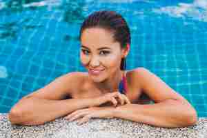 Bezpłatne zdjęcie portret pięknej azjatki w czarnym stroju kąpielowym w luksusowym basenie spa w kolczyku z piór sylish uśmiechnięta, seksowna, szczupła opalona ciało i mokra skóra, akcesoria w stylu letnim,