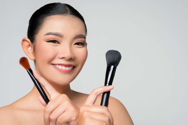 Portret pięknej azjatyckiej kobiety trzymającej pędzel do różu do makijażu