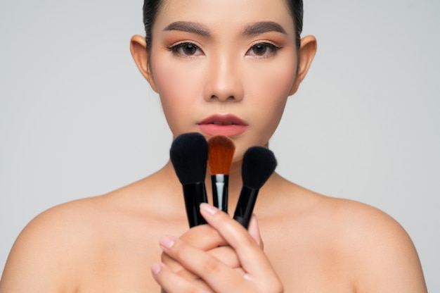 Portret pięknej azjatyckiej kobiety trzymającej pędzel do różu do makijażu