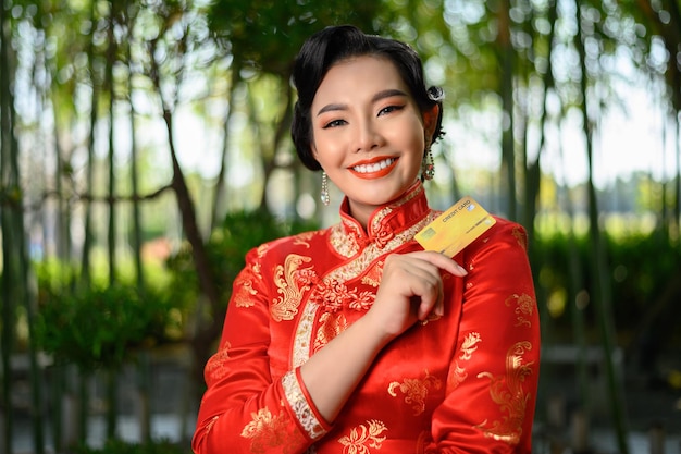 Portret pięknej azjatyckiej kobiety w chińskiej pozie cheongsam z kartą kredytową w bambusowym lesie