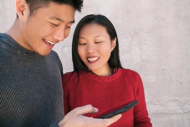 Portret pięknej azjatyckiej pary patrząc na telefon komórkowy, spędzając razem miło czas.