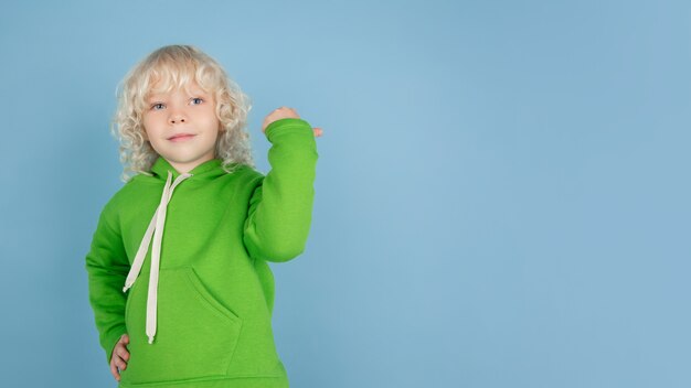 Portret pięknej kaukaski chłopczyk na białym tle na niebieskim tle studio. Blondynka kręcone męski model. Pojęcie wyrazu twarzy, ludzkich emocji, dzieciństwa, reklamy, sprzedaży.