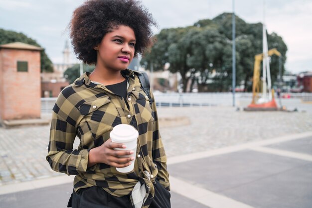 Portret pięknej kobiety afro amerykański Łacińskiej trzymając filiżankę kawy na zewnątrz na ulicy. Koncepcja miejska.