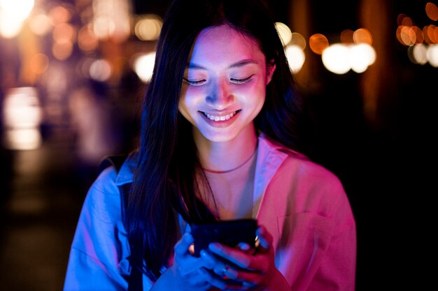 Portret pięknej kobiety przy użyciu smartfona w nocy w światłach miasta