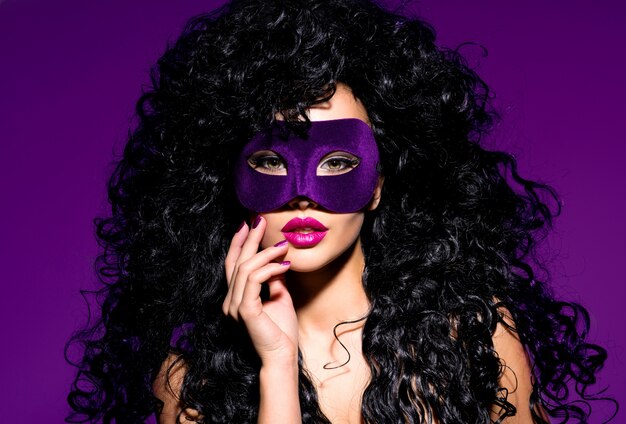 Portret pięknej kobiety z czarnymi włosami i fioletową maską teatralną na twarzy. Fioletowe paznokcie.