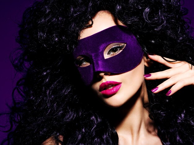 Portret pięknej kobiety z czarnymi włosami i fioletową maską teatralną na twarzy.