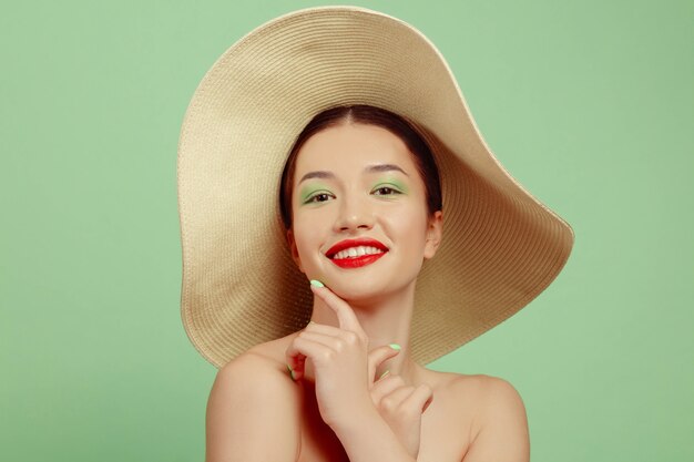 Portret pięknej kobiety z jasny makijaż i kapelusz na zielonej przestrzeni. Stylowa i modna marka i fryzura. Kolory lata