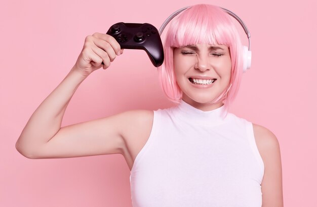 Portret pięknej kobiety z różowymi włosami, grając w gry wideo za pomocą joysticka w studio