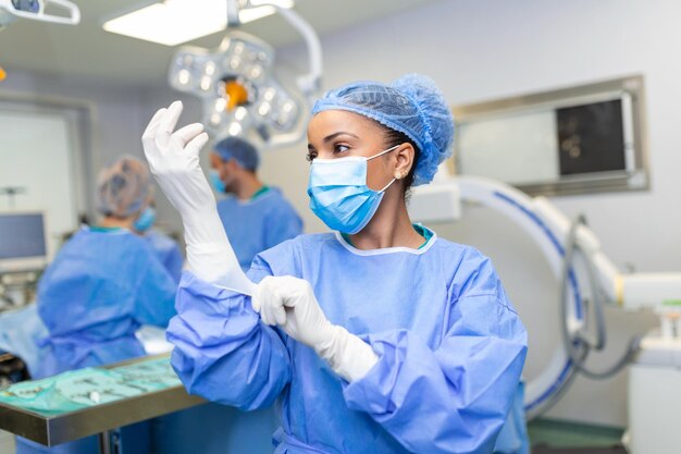 Portret pięknej lekarki chirurg zakładającej rękawiczki medyczne stojącej w sali operacyjnej Chirurg w nowoczesnej sali operacyjnej