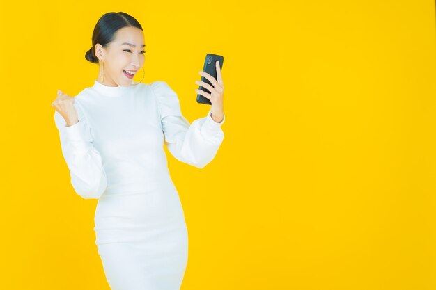 Portret pięknej młodej azjatyckiej kobiety uśmiech z inteligentnym telefonem komórkowym na żółto