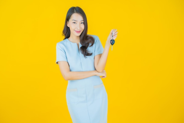 Portret pięknej młodej azjatyckiej kobiety uśmiech z kluczykiem na żółtym tle koloru