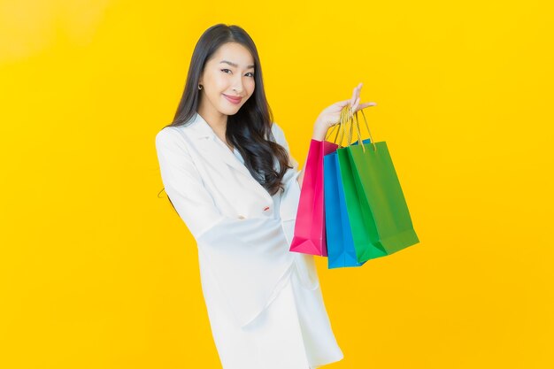 Portret pięknej młodej azjatyckiej kobiety uśmiech z torbami na zakupy na żółtej ścianie