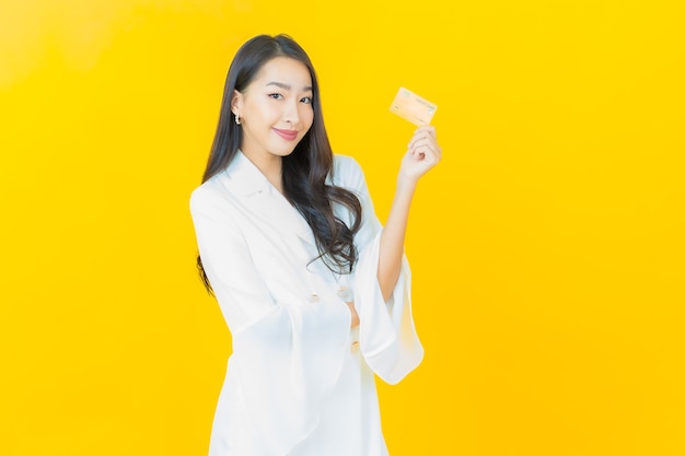 Portret pięknej młodej azjatyckiej kobiety uśmiecha się kartą kredytową na żółtej ścianie
