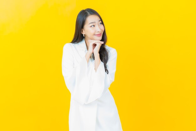Portret pięknej młodej azjatyckiej kobiety uśmiecha się na żółtej ścianie
