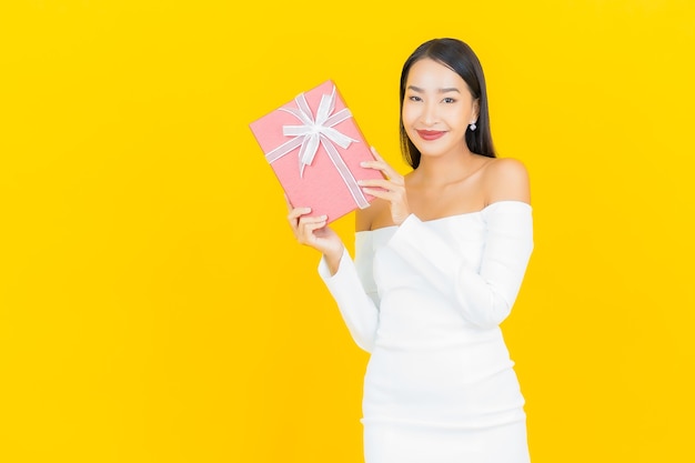 Portret pięknej młodej kobiety asian biznesu z czerwonym pudełkiem na żółtej ścianie