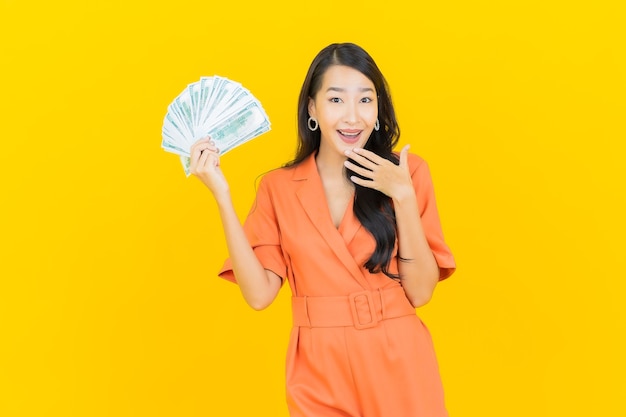 Portret pięknej młodej kobiety azjatyckiej uśmiech z dużą ilością gotówki i pieniędzy na żółto