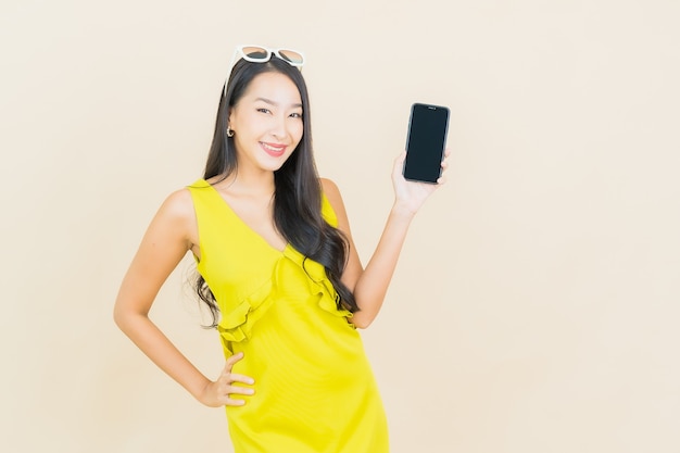 Portret pięknej młodej kobiety azjatyckiej uśmiech z inteligentny telefon komórkowy na kolorowej ścianie