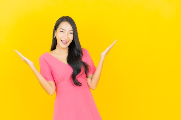 Portret pięknej młodej kobiety Azji uśmiecha się w różowej sukience na żółtej ścianie