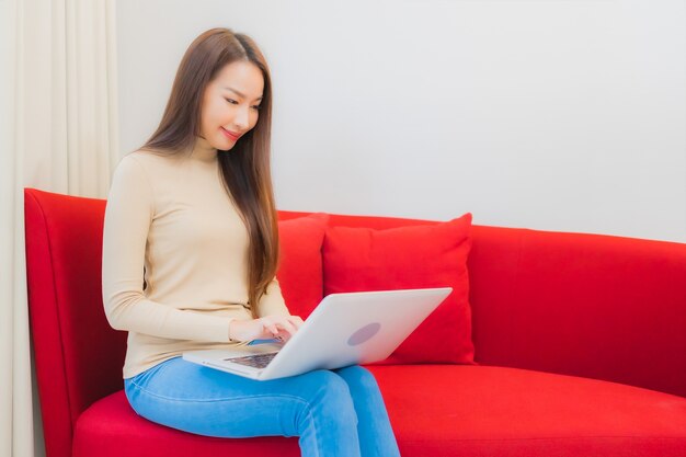 Portret pięknej młodej kobiety Azji używa komputera laptop na kanapie we wnętrzu salonu