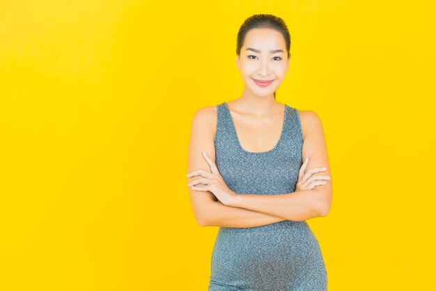 Portret pięknej młodej kobiety Azji z odzieży sportowej gotowy do ćwiczeń na żółtej ścianie