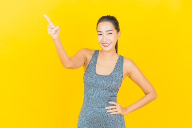 Portret pięknej młodej kobiety Azji z odzieży sportowej gotowy do ćwiczeń na żółtej ścianie