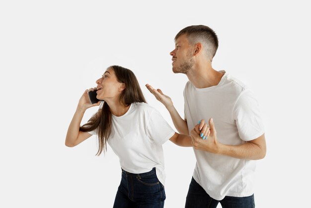 Portret pięknej młodej pary na białym tle na tle białego studia. Wyraz twarzy, ludzkie emocje, koncepcja reklamy. Kobieta rozmawia przez telefon, mężczyzna chce zwrócić na siebie uwagę.