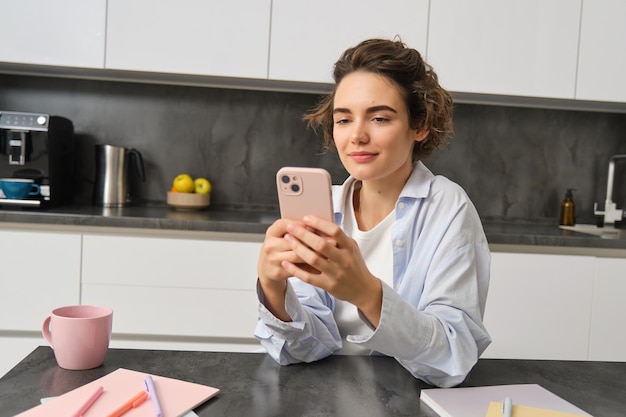 Portret pięknej uśmiechniętej kobiety siedzącej w domu ze smartfonem za pomocą aplikacji do telefonów komórkowych