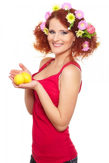 Portret pięknej uśmiechniętej rudzielec imbirowa kobieta w czerwonym płótnie z kolor żółty różowymi kolorowymi kwiatami w włosy odizolowywającym na bielu z cytryną w rękach