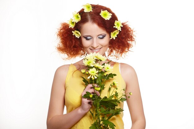 Portret pięknej uśmiechniętej rudzielec imbirowa kobieta w żółtym sukiennym mienie kolorze żółtym kwitnie i kwitnie w włosy odizolowywającym na bielu