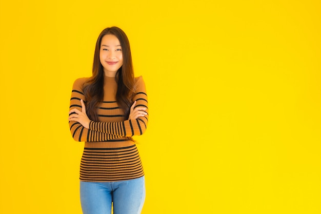 Portret piękny młody azjatykci dorosłej kobiety uśmiech z wiele akcją na kolor żółty ścianie