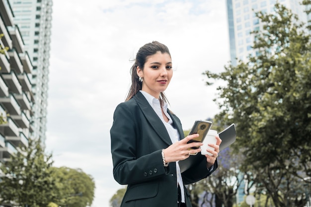 Portret piękny młody bizneswomanu mienia telefon komórkowy i rozporządzalna filiżanka