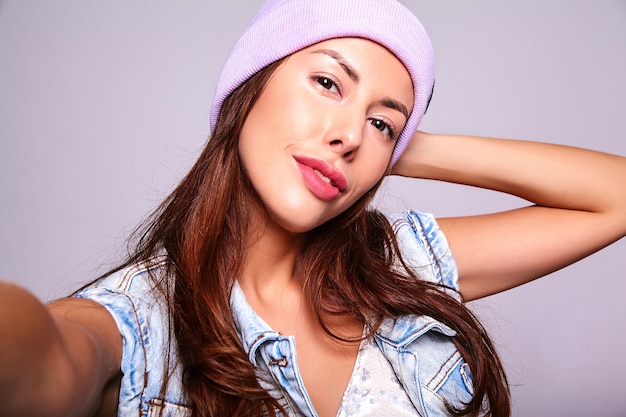 Portret Piękny śliczny Brunetki Kobiety Model W Przypadkowych Letnich Cajgach Odziewa Bez Makeup W Purpurowej Czapie Robi Selfie Fotografii Na Telefonie Odizolowywającym Na Szarość