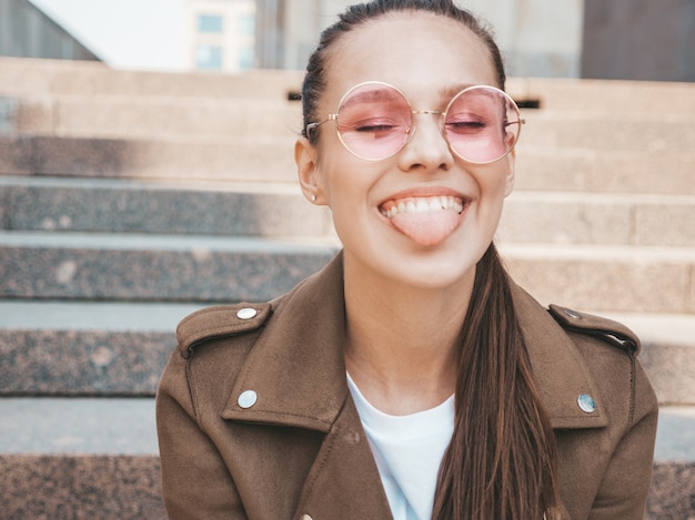 Portret piękny uśmiechnięty brunetka model ubierał w lato modnisia kurtki ubraniach pokazuje jej jęzor