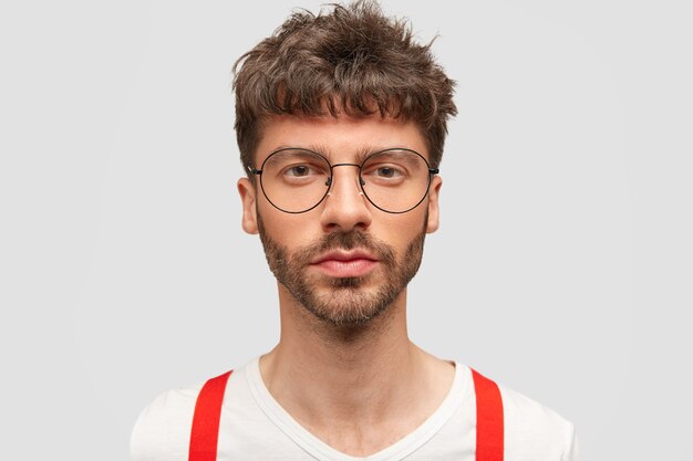 Portret poważnego atrakcyjnego studenta mężczyzny w okularach, elegancko ubranego, przychodzi na egzamin, pewny swojej wiedzy, pozuje na białej ścianie