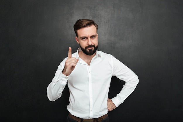 Portret poważny mężczyzna 30s w białej koszula pozuje na kamerze z pokazywać palec w górę odosobnionego nadmiernego zmroku - szarość