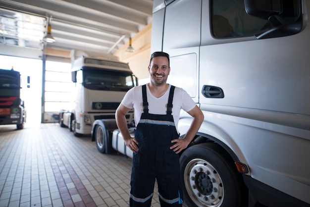 Portret pozytywny uśmiechnięty serwisant ciężarówka stojący przy pojeździe ciężarówki w warsztacie