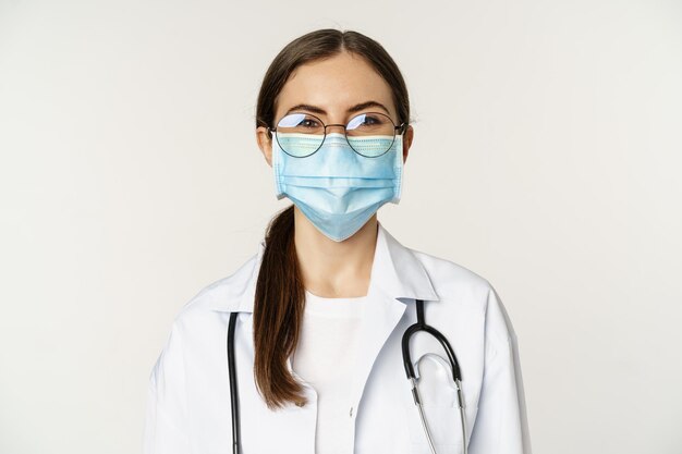 Portret pracowniczki medycznej kobiety lekarz w masce na twarz z covid podczas pandemii uśmiecha się i wygląda...