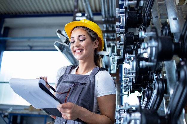 Portret pracowniczki przemysłowej w mundurze roboczym i kasku piszącym wyniki produkcji w fabryce