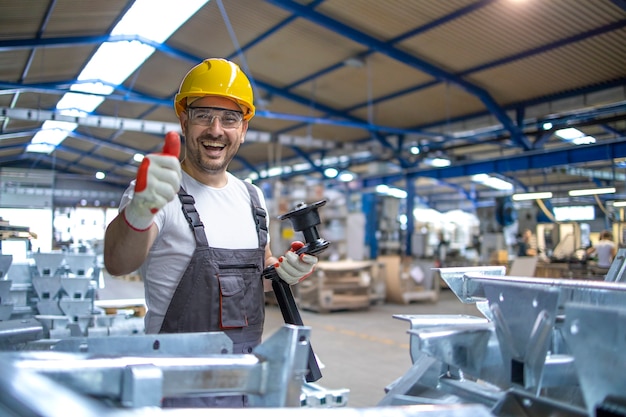 Portret pracownika fabryki w sprzęt ochronny, trzymając kciuki do góry w hali produkcyjnej