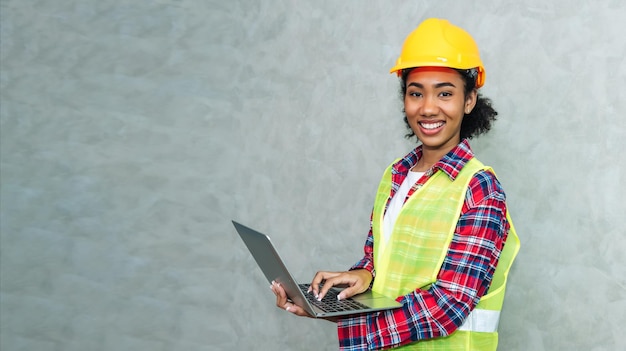 Portret profesjonalnej młodej czarnej kobiety inżynier budowlany pracownik architektury noszący kask ochronny do pracy na placu budowy lub w magazynie przy użyciu laptopa do pracy