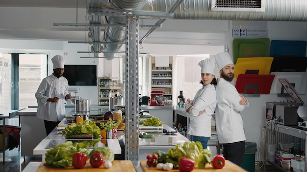 Bezpłatne zdjęcie portret profesjonalnych kucharzy pozujących z rękami skrzyżowanymi na aparacie, pracujących w kuchni restauracji, aby zrobić danie. mężczyzna i kobieta w mundurze będąc profesjonalnymi kucharzami, przygotowującymi kulinarny przepis.