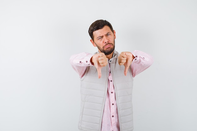 Portret przystojnego mężczyzny pokazujący kciuki w dół w kamizelce, koszuli i wyglądający na niezadowolonego