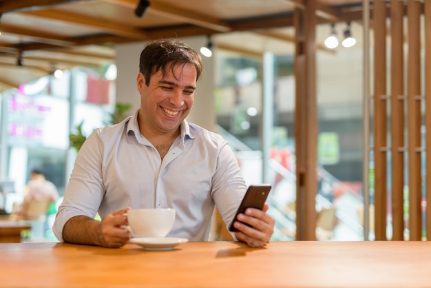 Portret przystojnego perskiego mężczyzny siedzącego w kawiarni podczas korzystania z telefonu komórkowego