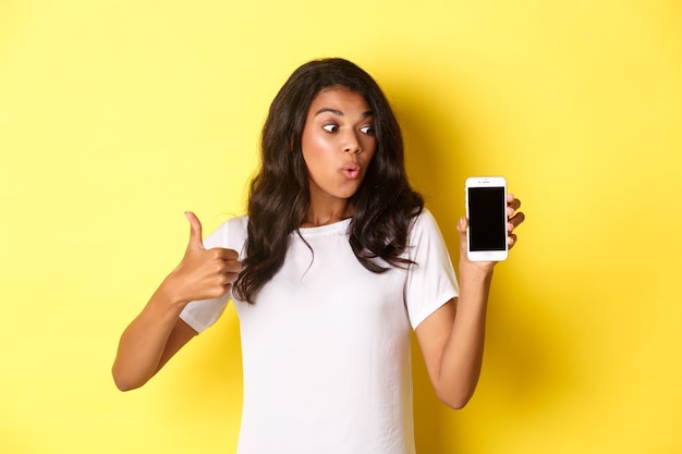 Portret przystojnej afroamerykańskiej modelki polecającej aplikację pokazującą telefon komórkowy