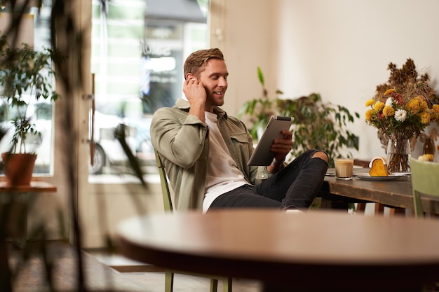 Portret przystojniaka szczęśliwego młodego mężczyzny siedzącego w kawiarni oglądającego filmy na cyfrowym tabletie