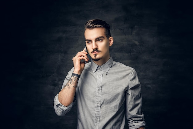 Portret przystojny brodaty mężczyzna hipster z tatuażem na ramieniu rozmawia na smartfonie.